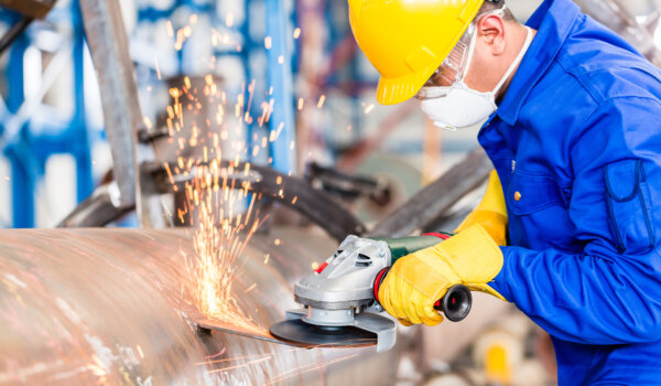 Metal worker in factory grinding metal of pipeline